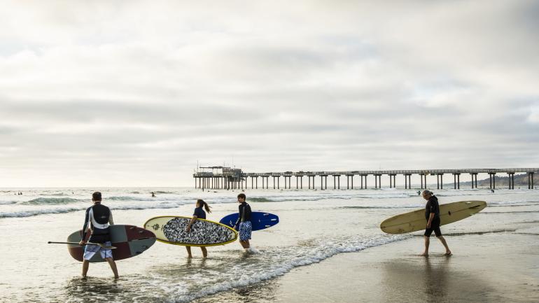 Surfistas e praticantes de stand-up paddle seguem para a água perto de Scripps Pier (Píer Scripps), em San Diego. Vistas dos surfistas remando nas ondas para aumentar o apelo da refeição a beira-mar. Surfistas e praticantes de stand-up paddle seguem para a água perto de Scripps Pier (Píer Scripps), em San Diego. Vistas dos surfistas remando nas ondas para aumentar o apelo da refeição a beira-mar.
