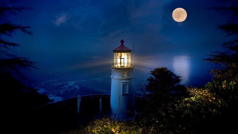 The illuminated Heceta Head Lighthouse, framed by a full moon The illuminated Heceta Head Lighthouse, framed by a full moon