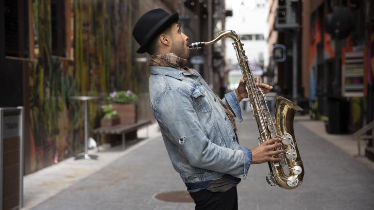 Omar Aragones playing the saxophone in The Belt, an alleyway filled with street art Omar Aragones playing the saxophone in The Belt, an alleyway filled with street art