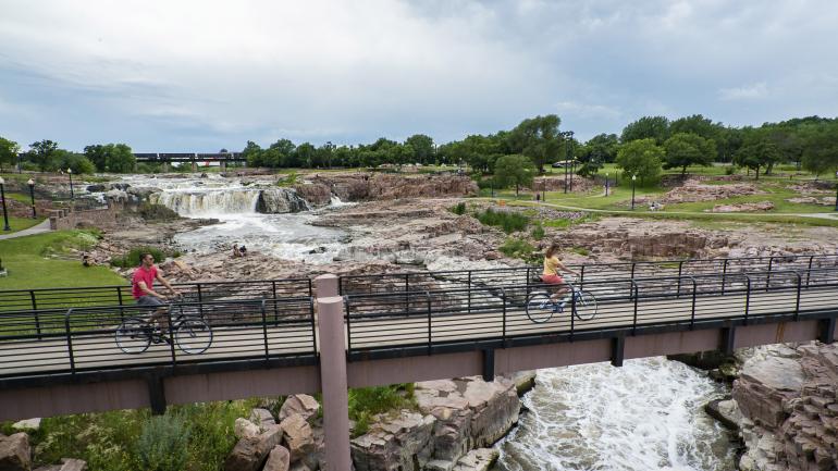 Biking across a bridge over the waterfalls of Falls Park in Sioux Falls, South Dakota Biking across a bridge over the waterfalls of Falls Park in Sioux Falls, South Dakota