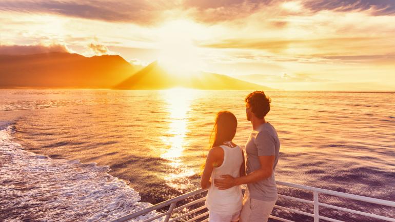 Una pareja admirando la puesta de sol mientras navegan por la costa de Maui Una pareja admirando la puesta de sol mientras navegan por la costa de Maui