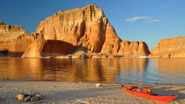 A kayak parked on the shore of Lake Powell with sandstone cliffs in the background A kayak parked on the shore of Lake Powell with sandstone cliffs in the background