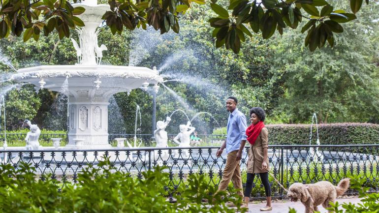 Couple walking a dog past Forsyth Park's iconic fountain in Savannah, Georgia Couple walking a dog past Forsyth Park's iconic fountain in Savannah, Georgia