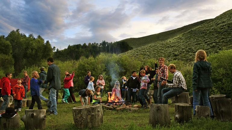 Families enjoying music by the campfire during a Colorado dude ranch stay Families enjoying music by the campfire during a Colorado dude ranch stay