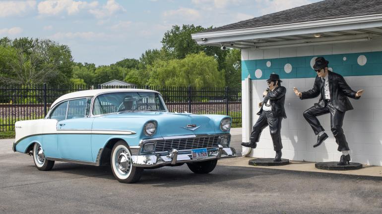Vintage Blue and White Car next to polka-dot building with two statues in suits. Vintage Blue and White Car next to polka-dot building with two statues in suits.