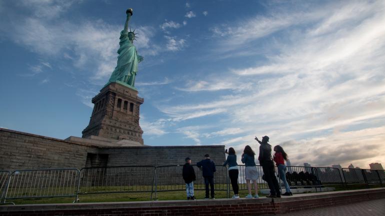 A group gazing up at the Statue of Liberty from the grounds of Liberty Island A group gazing up at the Statue of Liberty from the grounds of Liberty Island