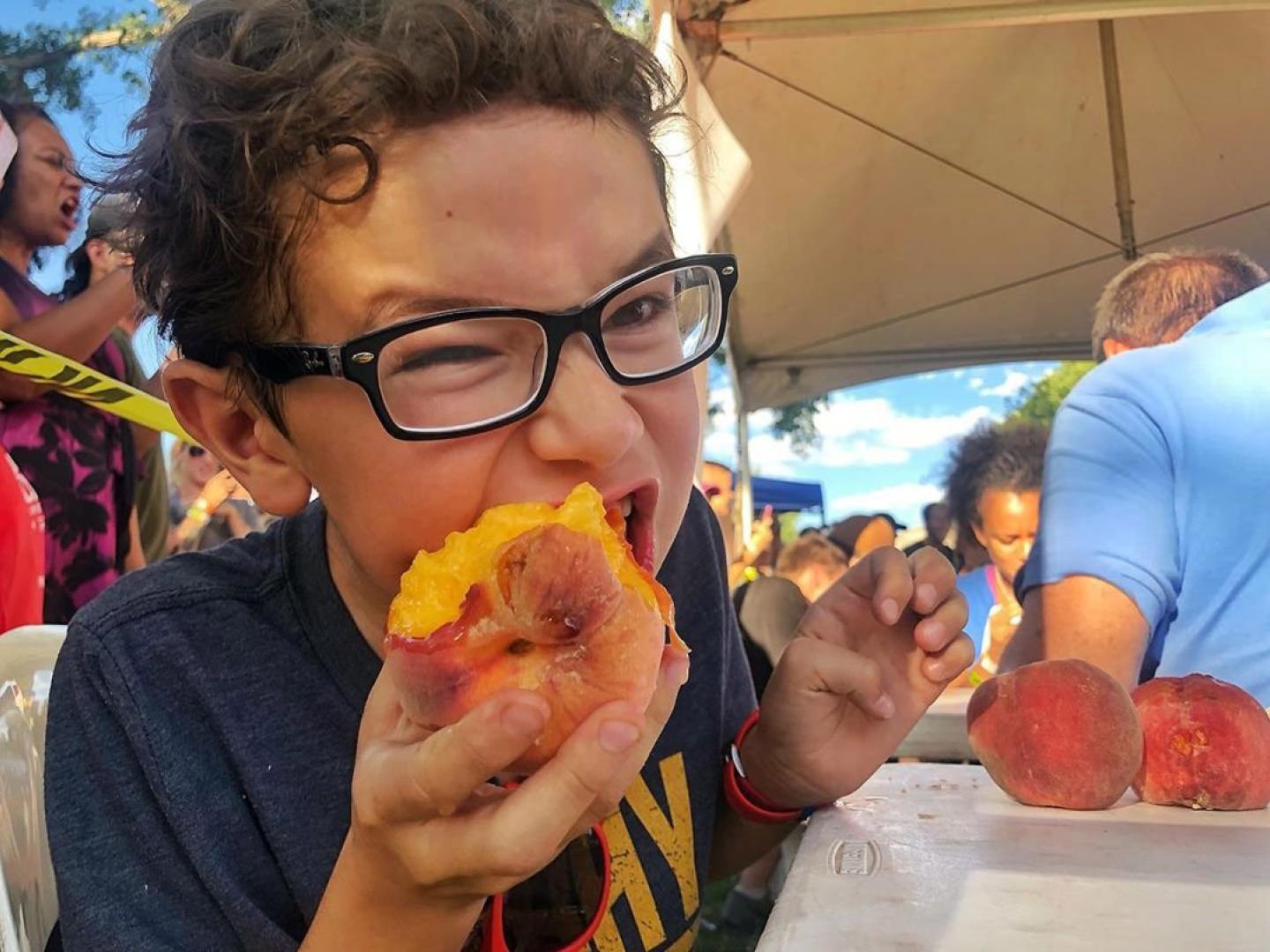 Ein Kind isst einen Pfirsich beim Palisade Peach Festival in Grand Junction, Colorado Ein Kind isst einen Pfirsich beim Palisade Peach Festival in Grand Junction, Colorado